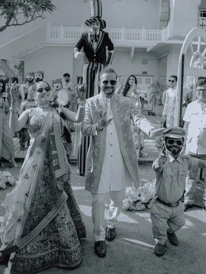 A fun, black and white shot of the couple's carnival-themed wedding entry, complete with performers on stilts, showcasing a unique and memorable celebration.