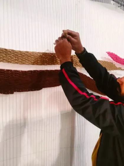 Another artist on my team working on the tapestry, carefully threading the yarn to create the abstract landscape.