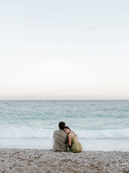 A serene scene on a pebble beach in Nice. This portrait of the couple looking out at the sea captures a feeling of peaceful love and shared dreams.