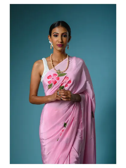 A beautiful studio portrait featuring a model in a hand-painted pink saree. The clean blue background makes the soft pink color stand out, perfect for a spring or summer collection.