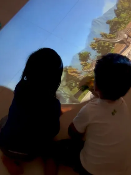 Two children watch dinosaurs roam across the floor, their silhouettes blending with the projection. This use of technology sparks a different kind of imaginative play, merging the digital and physical worlds.