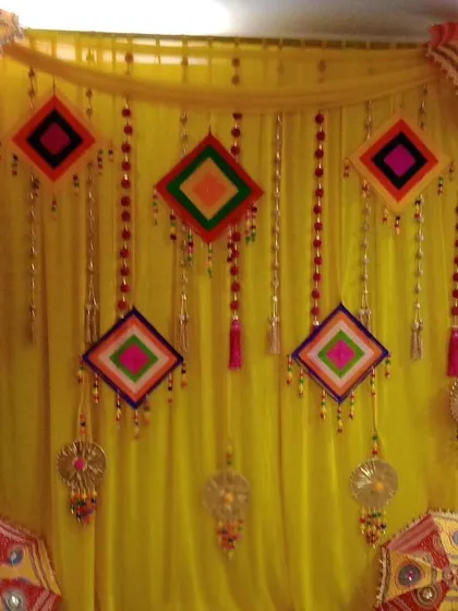 A detailed look at a Haldi backdrop featuring a yellow drape decorated with colorful hanging kites and dreamcatchers. This theme is perfect for a fun and youthful celebration.