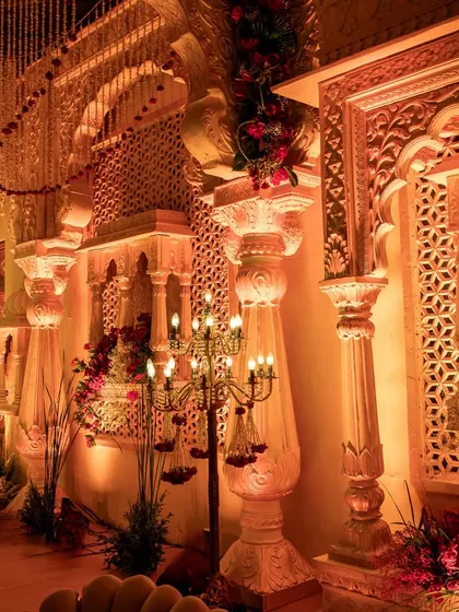 Intricately carved pillars and jaali work, illuminated by the warm glow of candelabras, create an atmosphere of ancient royalty and architectural beauty.