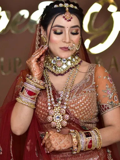 A bride adorned in a heavy, multi-layered bridal set featuring Polki stones and pearl detailing. The complete set includes a choker, long necklace, matha patti, nath, and bangles.