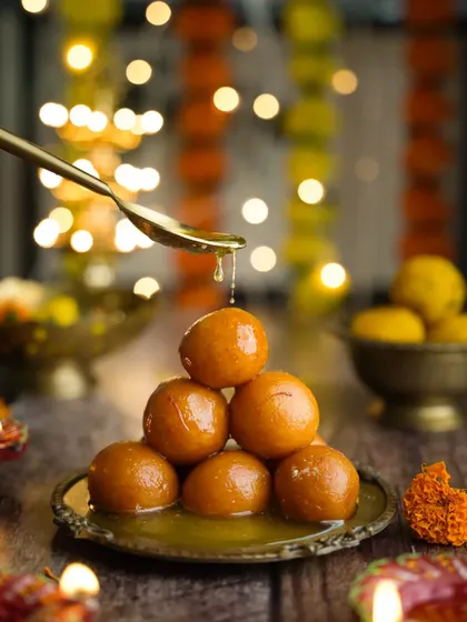 A pyramid of gulab jamuns against a backdrop of festive lights for Diwali. It’s a classic festive composition that feels warm, celebratory, and full of joy.