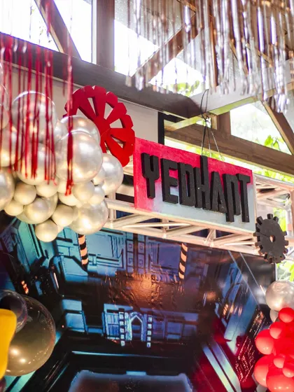 A close-up of the decor for a Transformers party. The setup includes a backdrop of a futuristic tunnel, silver balloon garlands, and gear-shaped cutouts, creating a sci-fi, industrial vibe.