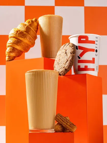A styled product shoot for Flyp Coffee, featuring their coffee and baked goods. The use of geometric blocks and a bold orange color palette creates a modern and energetic brand look.