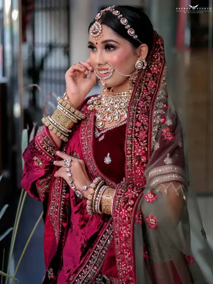 A smiling, three-quarter portrait of the bride. The natural outdoor lighting creates a soft and flattering look, enhancing the rich colors of her velvet lehenga.
