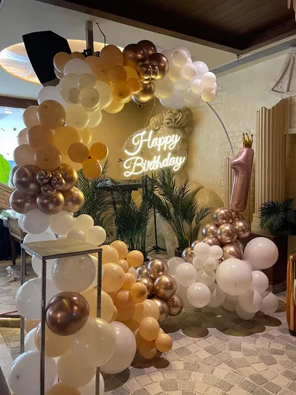 A beautiful and soft-toned balloon arch in peach, white, and rose gold. This setup, complete with a neon sign and a number '1' balloon, is perfect for a first birthday or baby shower.