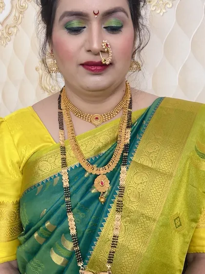 A beautiful look featuring a green saree with a yellow blouse. The makeup is highlighted by green eyeshadow that matches the saree, a traditional `nath`, and classic gold jewellery.