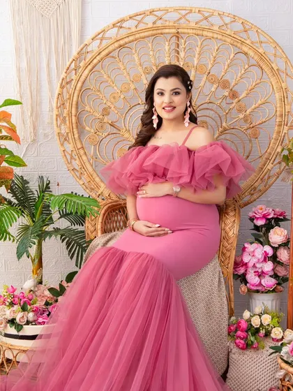 Seated on a grand peacock chair, this mother-to-be looks like royalty in a vibrant pink mermaid gown. The surrounding floral arrangements in matching tones create a lush, romantic scene.