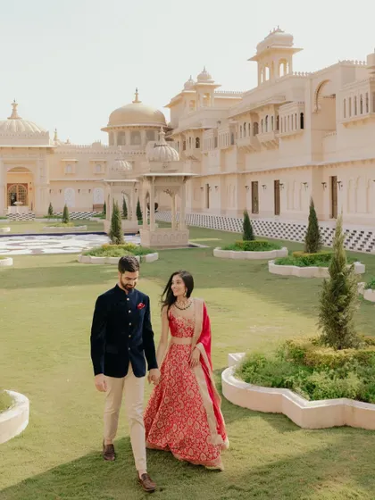 A romantic shot of Nikita and Rishabh walking through the gardens of the Udaivilas. The grandeur of the palace in the background adds to the fairytale feel.