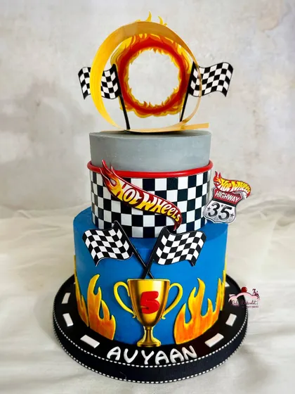 A three-tier Hot Wheels cake for an epic 5th birthday. It's designed to look like a race track with checkered flags, flames, and a ring of fire topper.