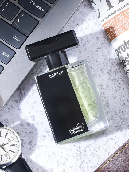 A masculine flatlay for 'Dapper' perfume, set on a desk with a laptop, watch, and newspaper. This lifestyle context clearly targets the modern working professional.