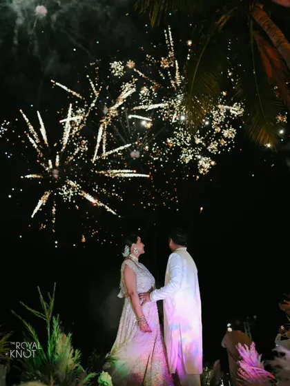 The couple watches as fireworks light up the night sky over the palm trees at their destination wedding in Thailand.