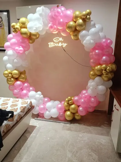 A "Welcome Baby" ring decoration in a bedroom. This pink, white, and gold balloon arch with an "Oh Baby" neon sign is a sweet way to welcome a new family member.