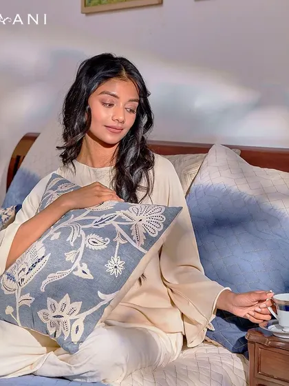 Discover the art of relaxation with my Indigo collection. Here, a woman enjoys a quiet moment with a cup of tea, surrounded by the soothing blue floral patterns of my designer cushions.
