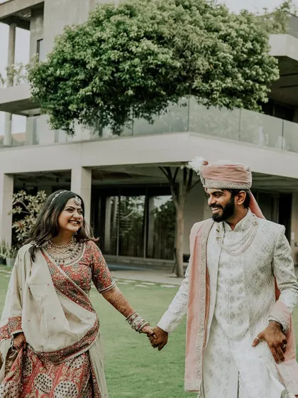 A joyful walk in the garden. The couple's smiles and hand-in-hand stroll capture the easy, happy love they share, set against the modern architecture of their wedding venue.