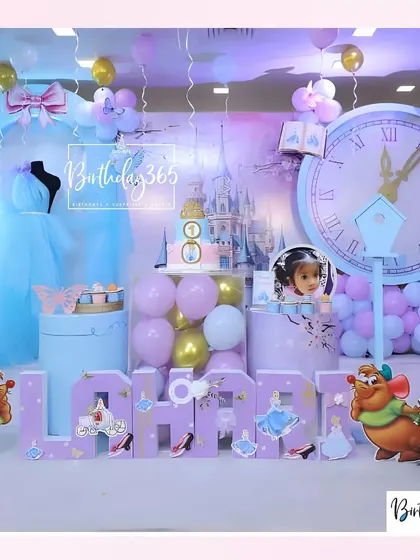 A full view of the Cinderella stage setup, showcasing the large clock striking midnight, the castle backdrop, and personalized "Lahari" name blocks.