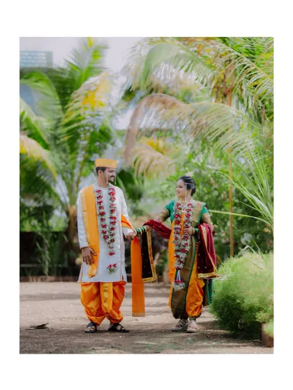 A full-length shot of the couple in their vibrant yellow and orange traditional Maharashtrian wedding attire, walking hand-in-hand.