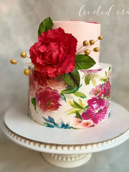 This two-tiered cake combines modern elegance with artistry. The bottom tier is wrapped in a printed floral design, complemented by a large, handmade red sugar peony that adds a touch of drama.