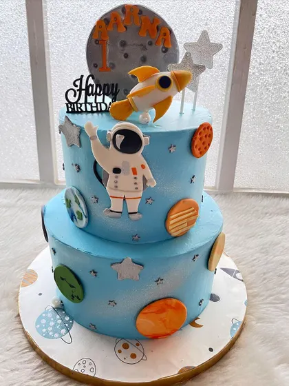 The full view of the two-tier space adventure cake. The blue frosting is airbrushed to look like a galaxy, creating a perfect backdrop for the planets and astronaut.