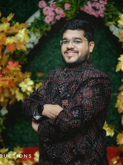 A handsome portrait of the groom-to-be at his engagement, posing in front of a festive floral arch.
