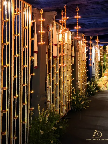 A beautiful walkway lined with panels of hanging diyas and floral strings, creating a grand and divine entrance for the event.