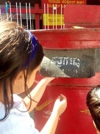 A child reaches up to post her letter in the bright red postbox. This tangible action was the exciting culmination of their field trip.