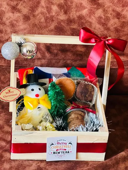 A charming Christmas hamper in a wooden basket. This gift includes a snowman figurine, a miniature Christmas tree, cookies, and other festive treats.