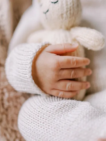 A close-up detail of a newborn's hand holding a tiny knitted bear, highlighting the delicate features and textures of the session.