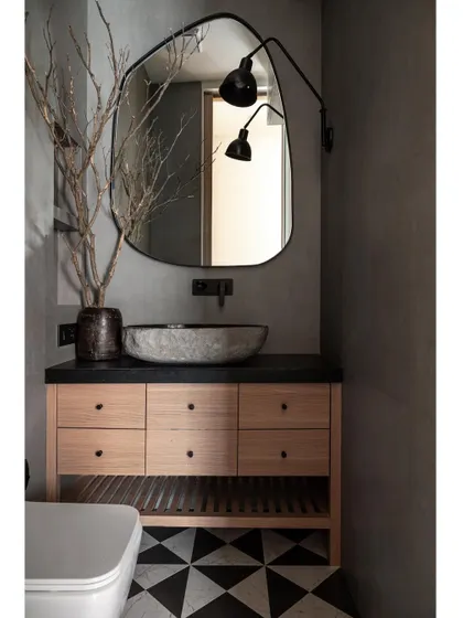 This chic powder bathroom features a black leather-finish marble basin counter that harmonizes with patterned flooring and fabric-finished wall tiles. A generously sized mirror enhances both elegance and the sense of spaciousness.