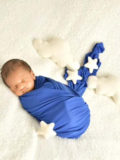 A sweet sleeping baby wrapped in blue, dreaming among soft, plushy stars and clouds. This simple themed setup adds a touch of whimsy to a classic newborn portrait.