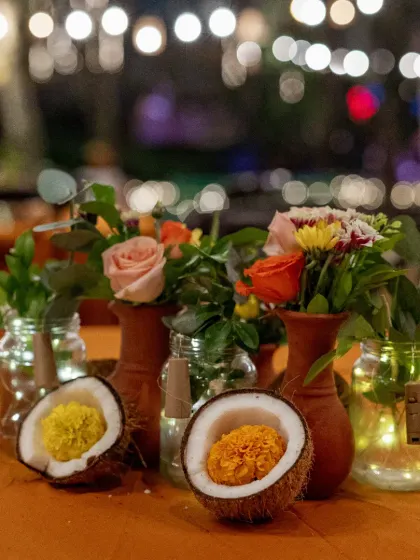 A creative and rustic centerpiece using terracotta pots, mason jars with fairy lights, and coconuts filled with marigolds for a unique table setting.