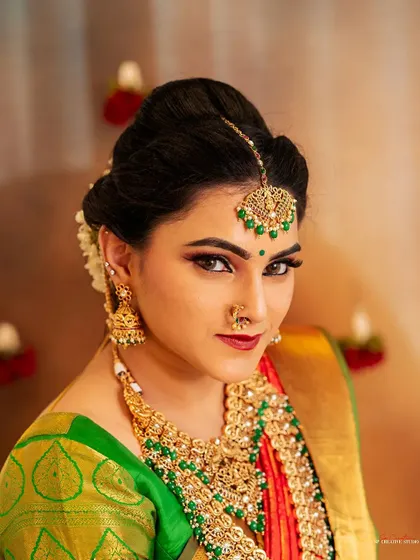 A striking close-up portrait from a styled shoot, highlighting the detailed makeup and green-beaded temple jewelry.
