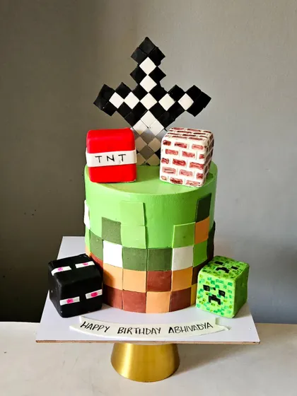 A pixel-perfect Minecraft cake. This design captures the blocky aesthetic of the game with a pixelated whipped cream finish and edible, hand-cut fondant blocks like TNT and Creeper.