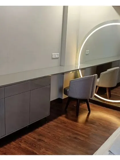 A custom-designed dressing table and storage unit in a soft grey finish, paired with a large, backlit circular mirror. This setup creates a functional and glamorous space for daily routines.
