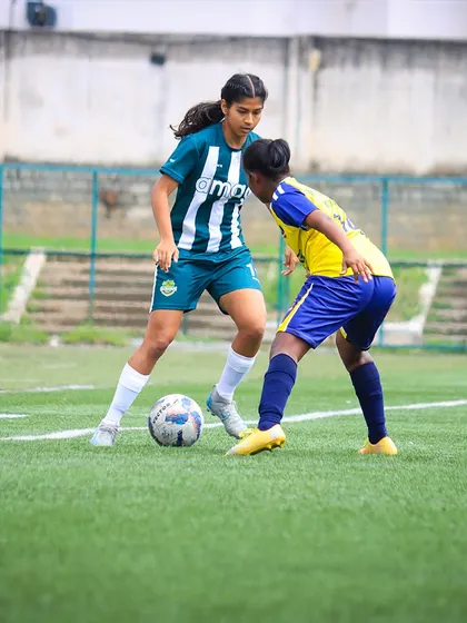 Close control and focus on display as a player maneuvers the ball under pressure from an opponent in a girls' league match.