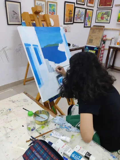 The painting progresses as the student fills in the iconic white buildings and deep blue sea of the Santorini scene, focusing on clean lines and color blocking.