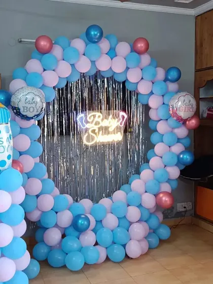 A 'Baby Shower' setup for a boy, with a circular balloon arch in blue and pink against a silver shimmer curtain.