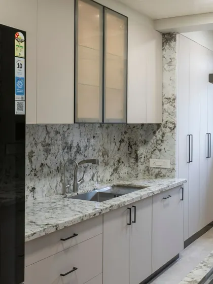 This kitchen uses a striking granite with dramatic veining for both the countertop and backsplash, creating a seamless and impactful look. The light grey cabinets provide a soft, neutral balance.