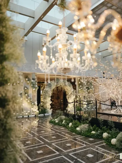 The grand entrance to an elegant sangeet, where crystal chandeliers and a lush floral archway create a breathtaking first impression. The design combines classic luxury with a modern aesthetic.