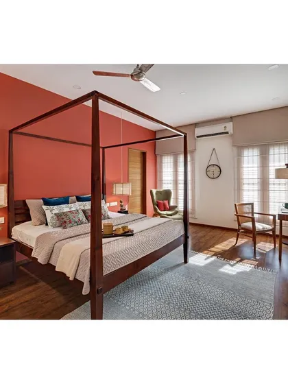 The master bedroom of the Nataraj House uses a warm terracotta accent wall to create a cozy and inviting atmosphere. The four-poster bed and cane pendant lights complete the tropical, down-to-earth feel.
