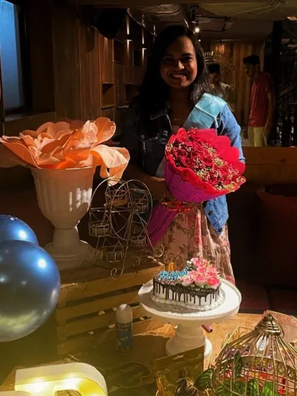 A happy client enjoying her birthday surprise. Holding a beautiful bouquet of red roses, she stands by the decorated table I prepared, complete with a custom cake and personal touches.
