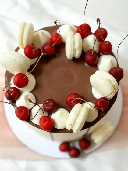 A top-down view of the cherry and macaron drip cake, showing the full arrangement of fruit and French macarons on a chocolate ganache top.