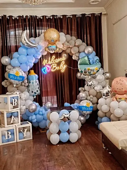 A full room decoration for a 'Welcome Baby' party. The setup includes a circular balloon arch, 'BABY' blocks, and various themed foil balloons like a baby bottle and a moon.
