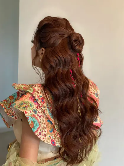 This textured top knot combined with loose waves is the ultimate mehendi hairstyle. The pink threads add a pop of color, while extensions ensure the hair looks full and festive.