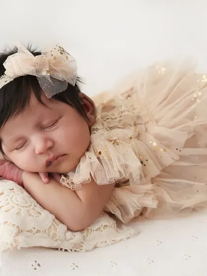 A dreamy portrait of a sleeping newborn. Dressed in a delicate tulle outfit and resting on a lace pillow, this image is all about soft textures and angelic details.