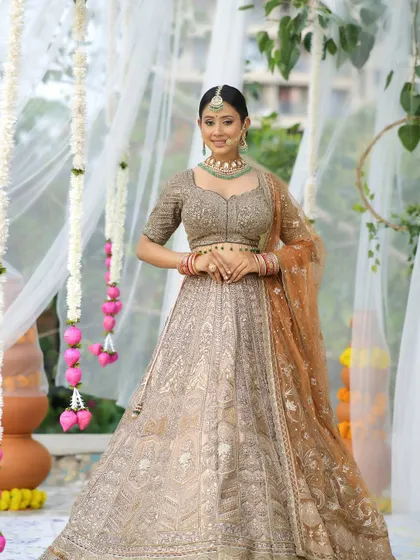 A full shot of the bride, highlighting the intricate work on her lehenga. The makeup is designed to complement the outfit without overpowering it.