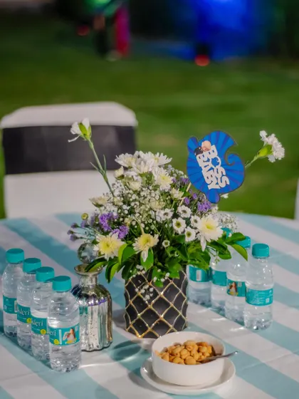 A simple yet thematic table centerpiece at a "Boss Baby" party. The floral arrangement is accented with a "Boss Baby" cutout, and the blue and white striped tablecloth matches the overall color scheme.